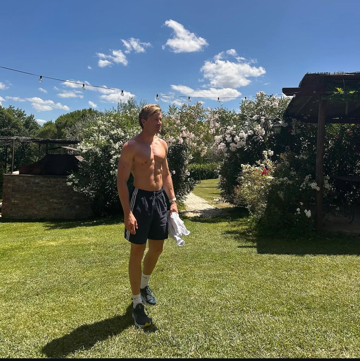 Man standing shirtless on a grassy lawn with a clear blue sky