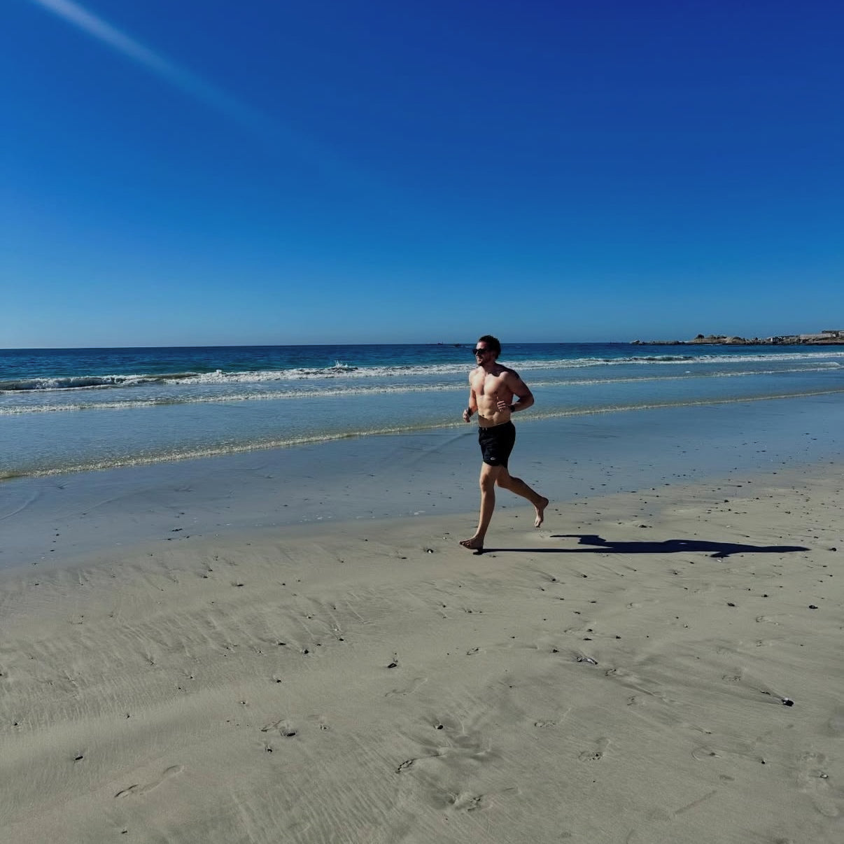 Man running on a sandy beach with clear blue sky and ocean in the background