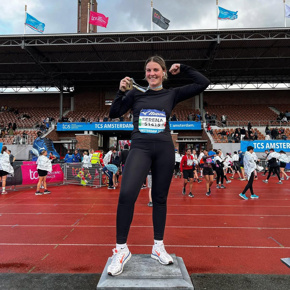 Woman celebrating on a track with 'TCS Amsterdam' branding in the background